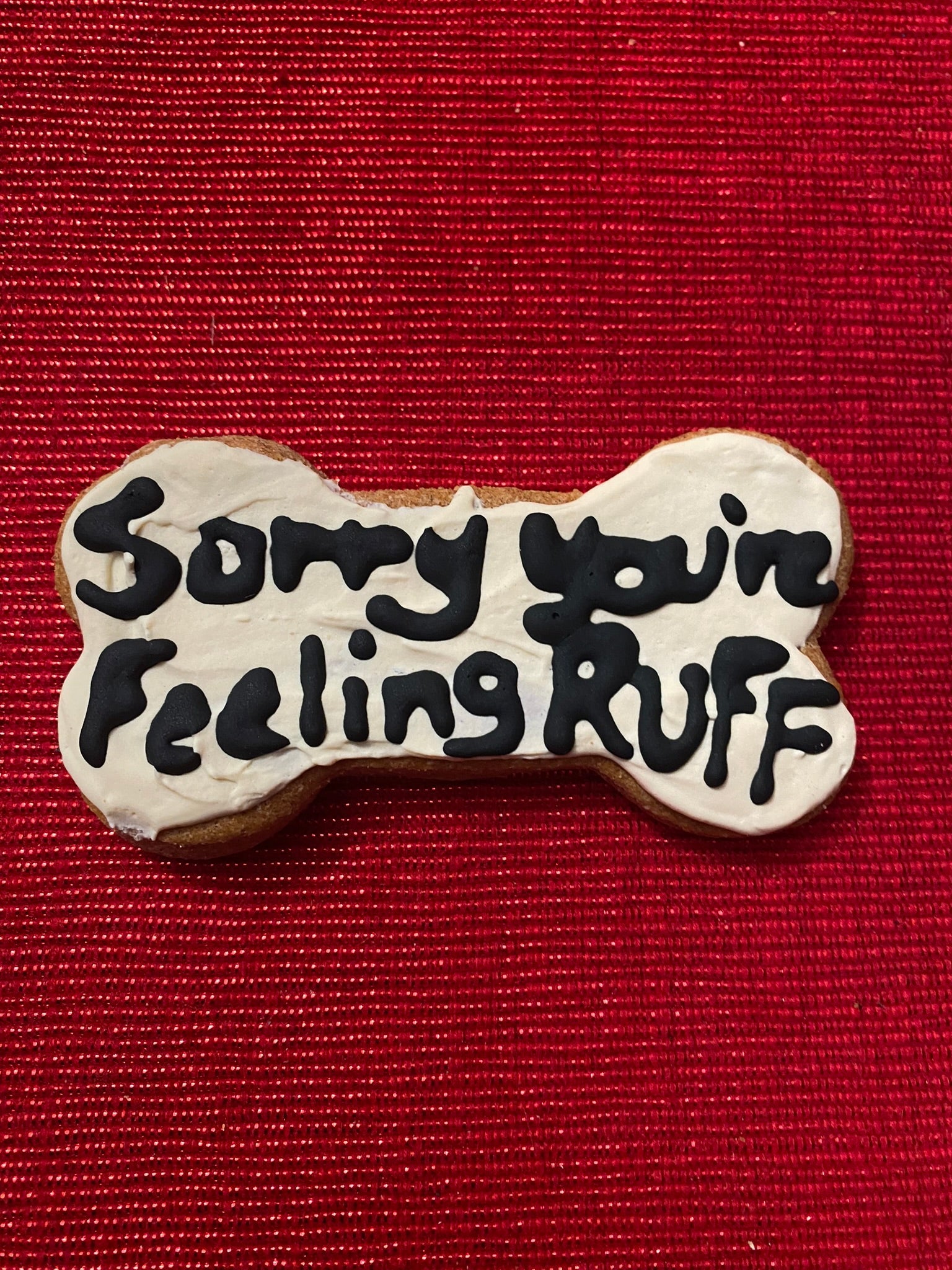 Dog bone-shaped cookie with 'Sorry your feeling ruff' text on a red background