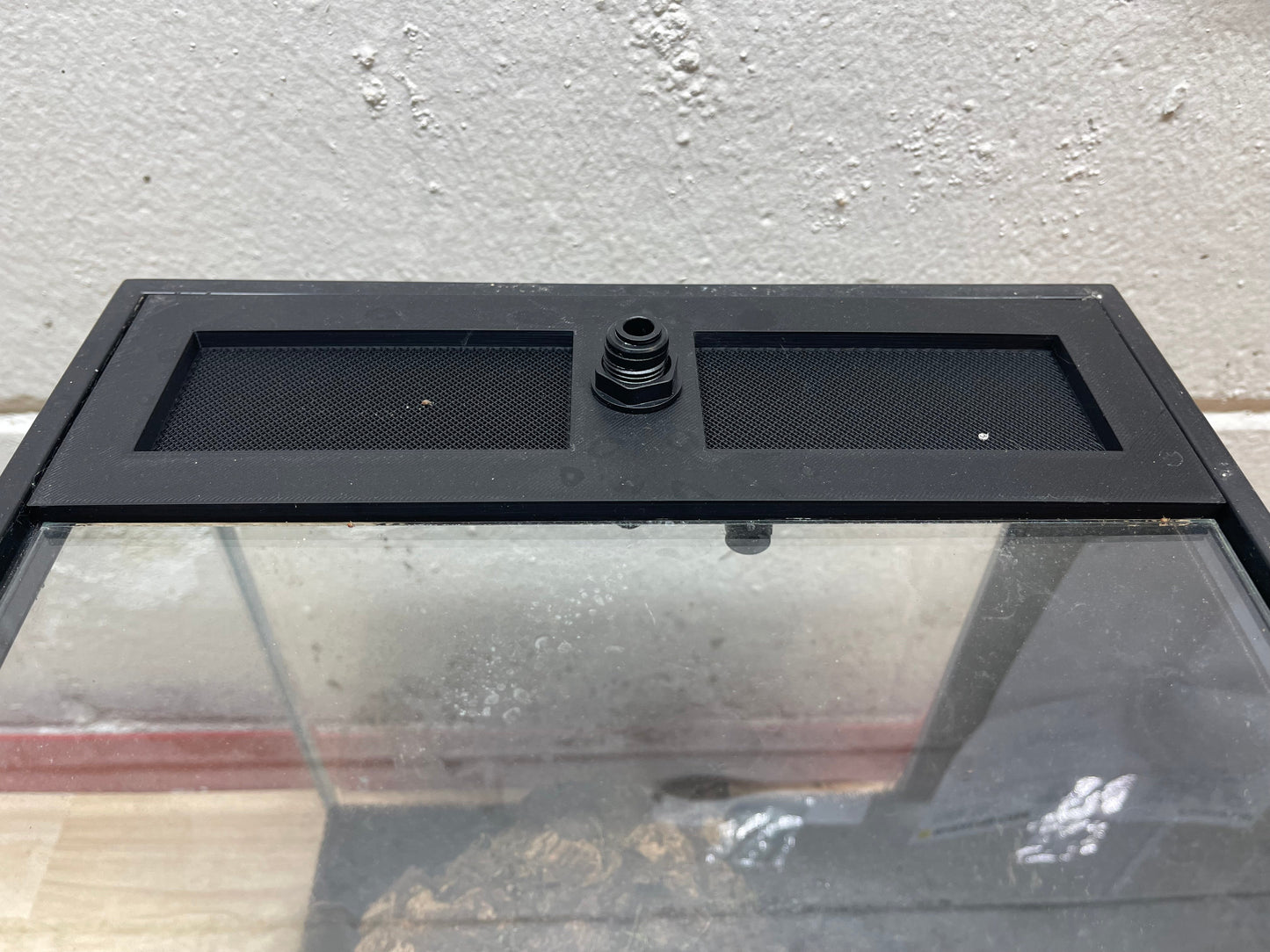 Black aquarium cover with a central vent on a reflective surface