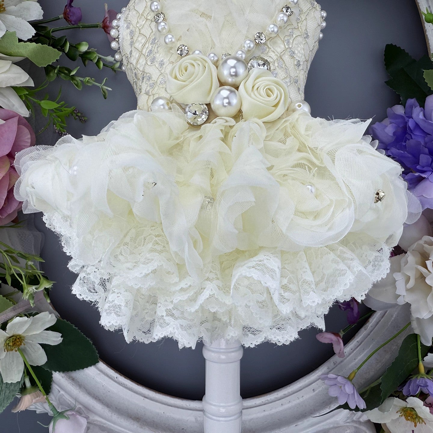 Decorative flower arrangement with white roses and pearls on a stand, surrounded by other flowers.
