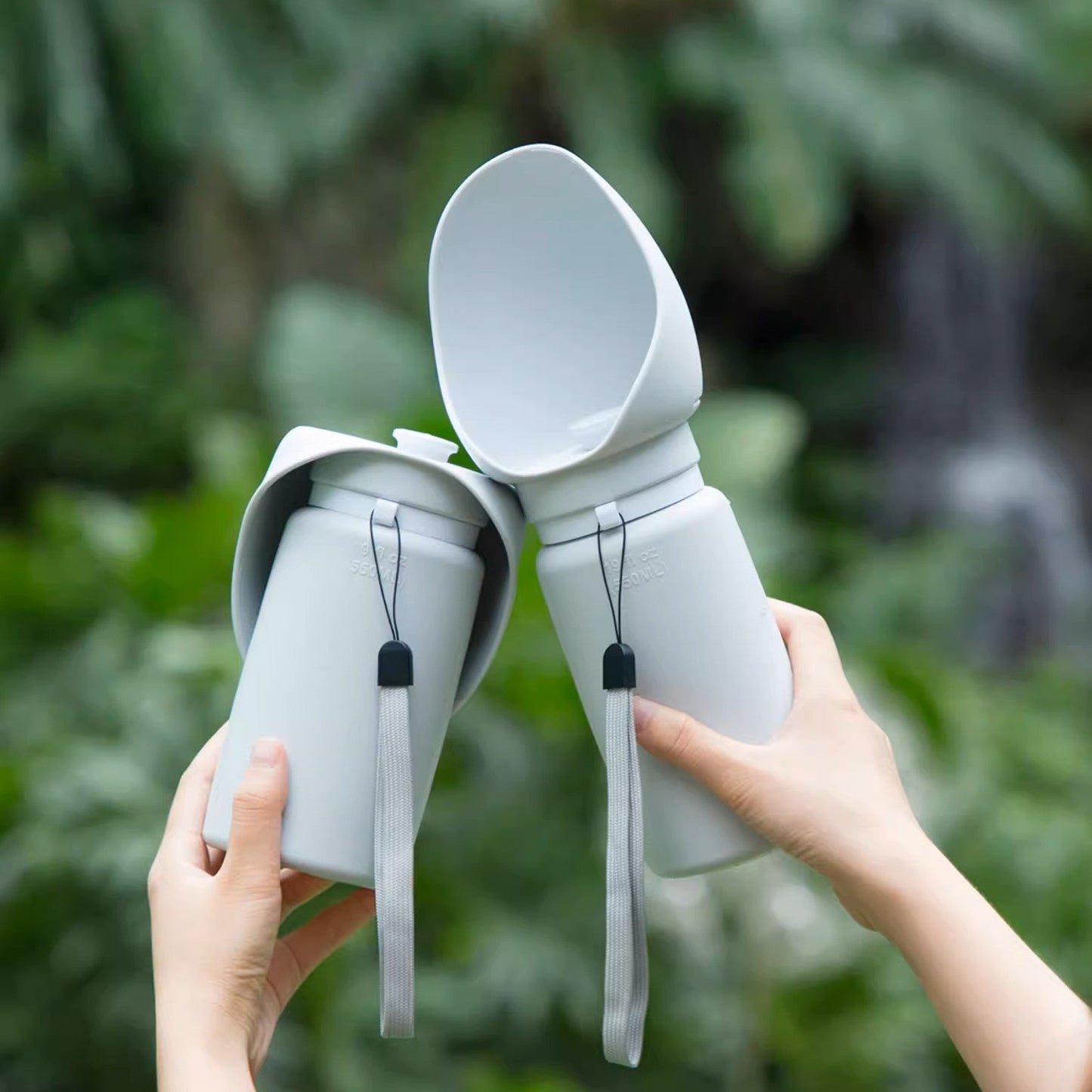 Two white ceramic cups with lids held by hands against a blurred green background