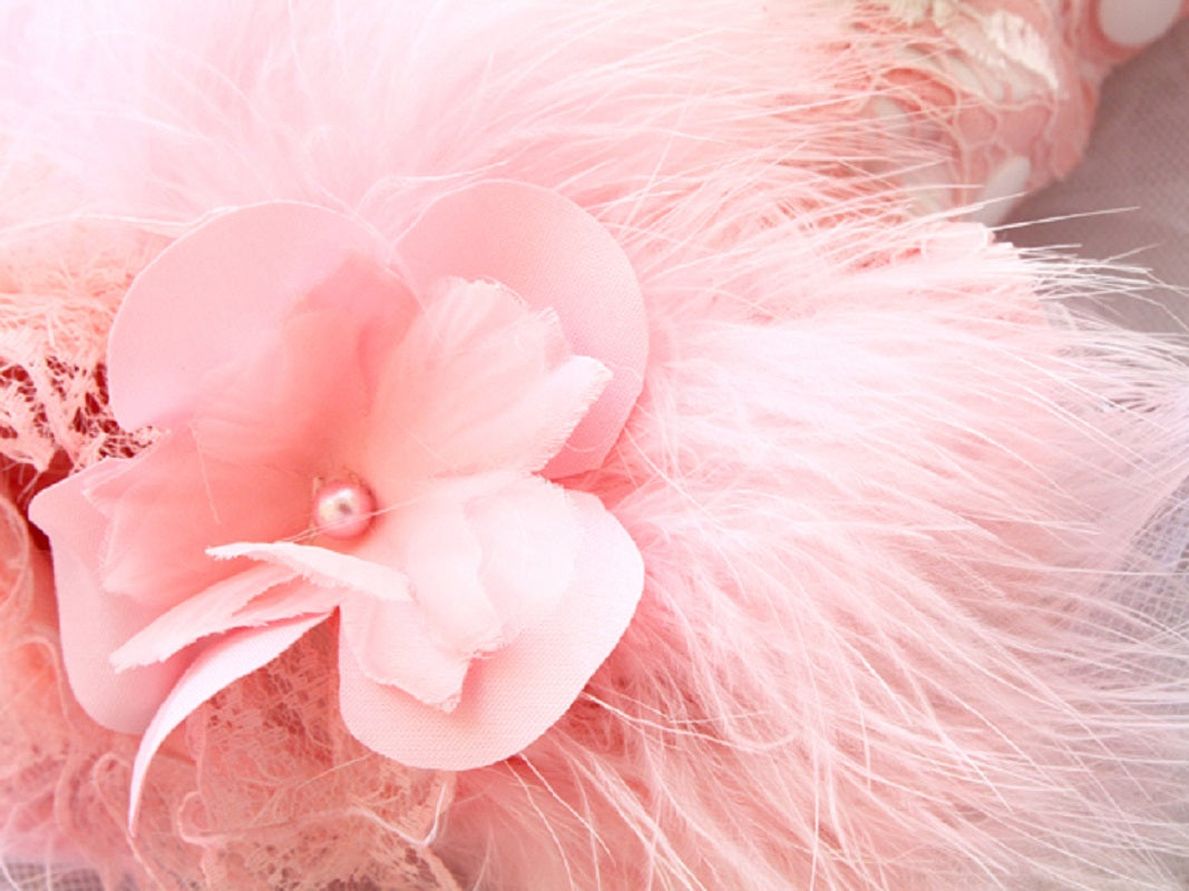 Close-up of a pink floral hair clip with feathers on a soft pink background