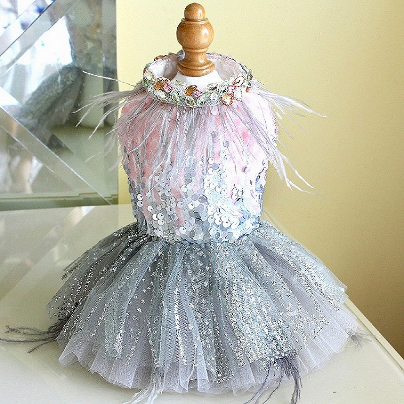Dress on a mannequin with sequins and feathers on a reflective surface.