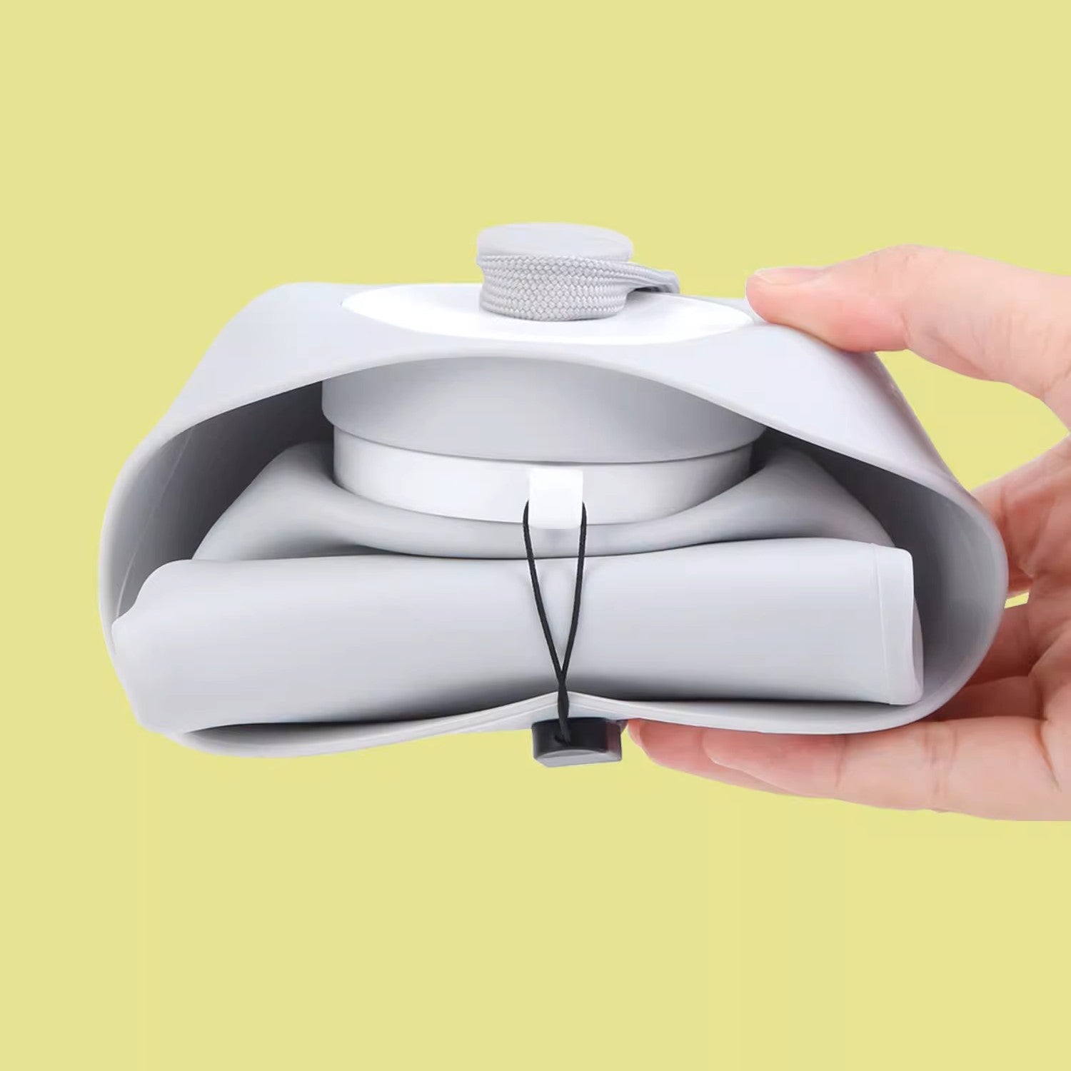 White travel case with a small white device inside, held by a hand against a yellow background