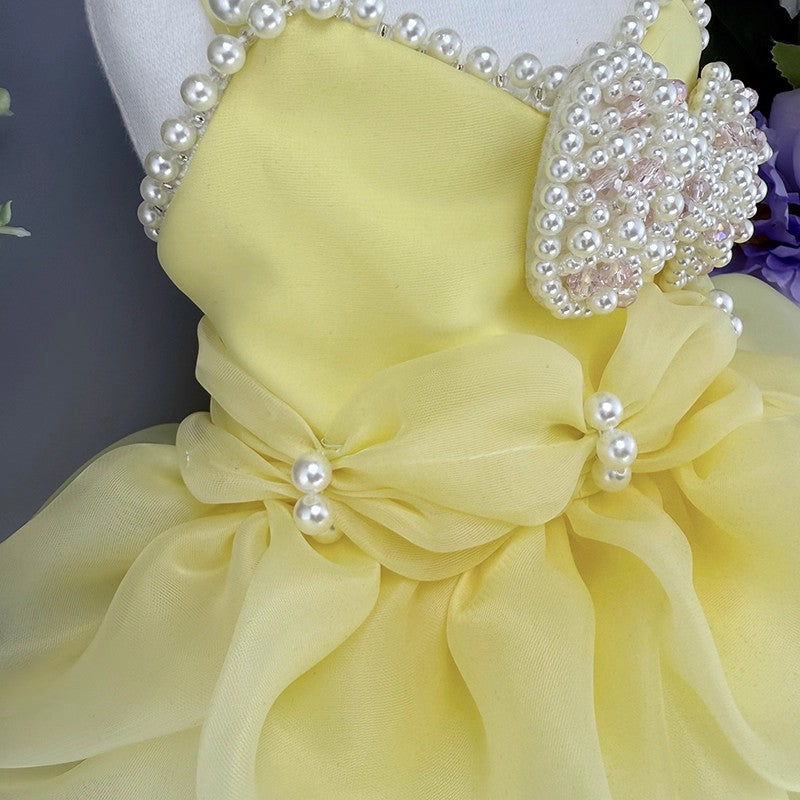 Yellow dress with large bow and pearl embellishments on a mannequin against a dark background