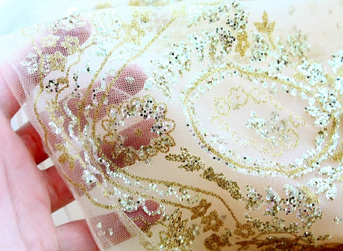 Close-up of decorative fabric with gold embroidery and glitter held by a hand.