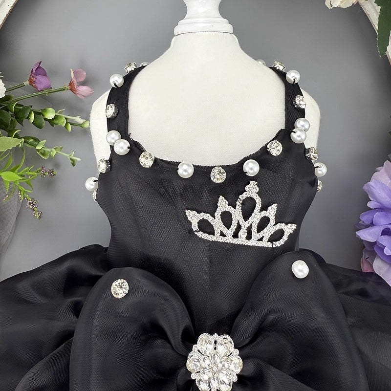 Black dress with decorative elements on a mannequin against a gray background with flowers.