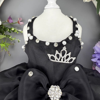 Black dress with decorative elements on a mannequin against a gray background with flowers.