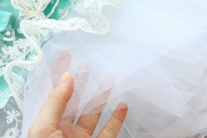 Close-up of a hand touching white tulle fabric with lace details in the background.