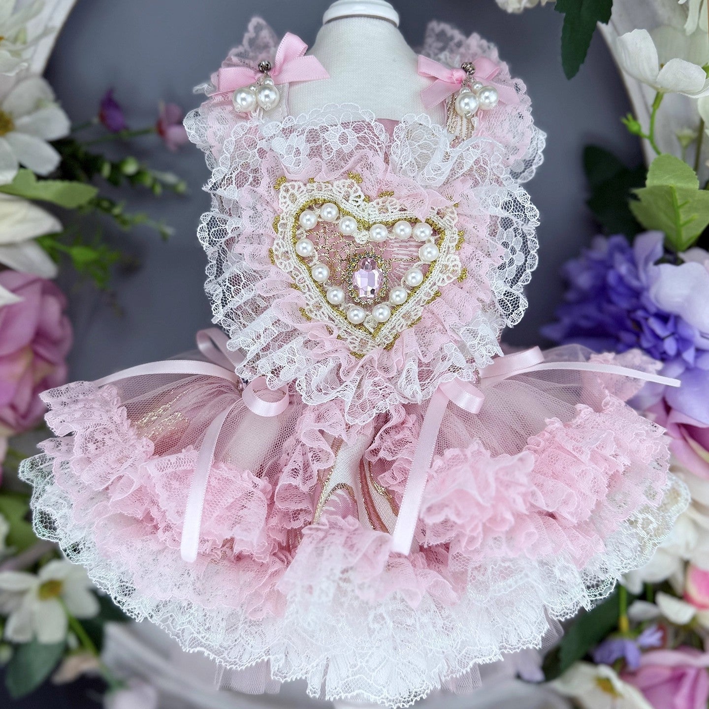 Pink and white lace pet dress with decorative heart on a mannequin against a floral background