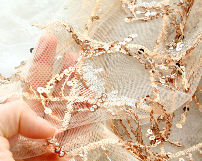 Close-up of decorative lace fabric with gold embroidery and a hand holding it.