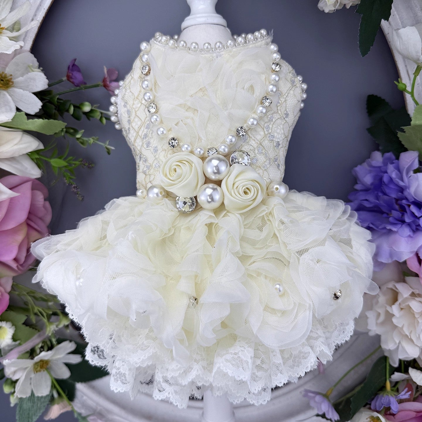Delicate white floral dress with pearls and lace on a mannequin against a floral background