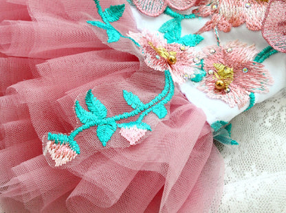 Close-up of a pink fabric with floral embroidery and tulle, on a textured surface.