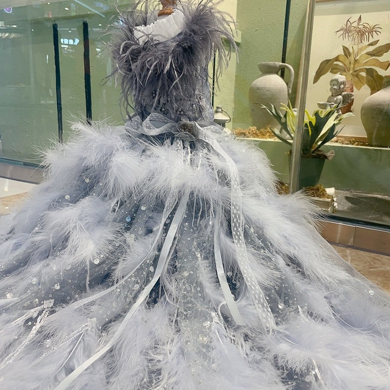 Mannequin wearing a decorative gown with white feathers and ribbons in a store setting.