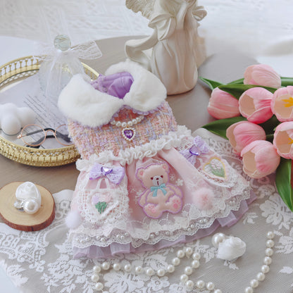 Delicate pink dress with teddy bear design on a lace tablecloth with flowers and jewelry.