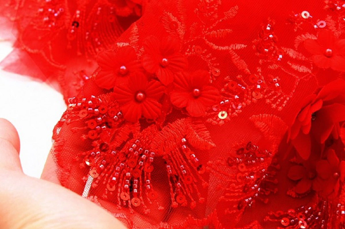Close-up of red floral lace fabric with beads held by a hand.
