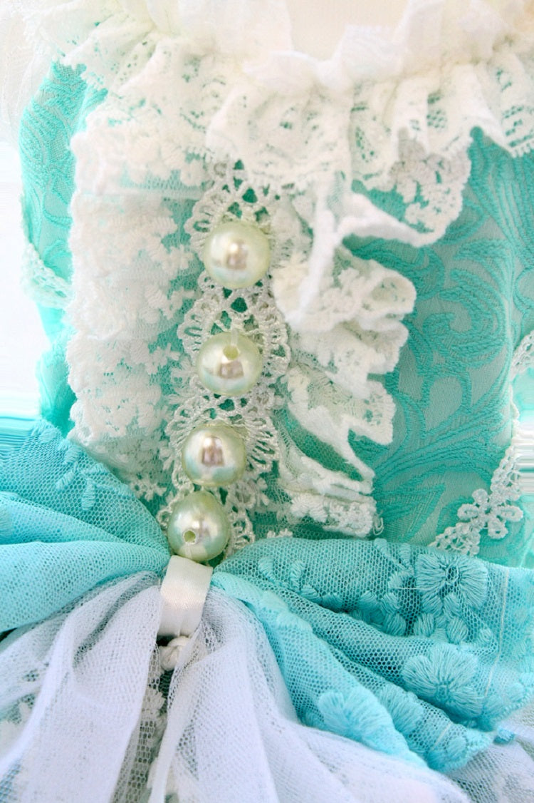 Close-up of a decorative item with lace, pearls, and tulle in teal and white.