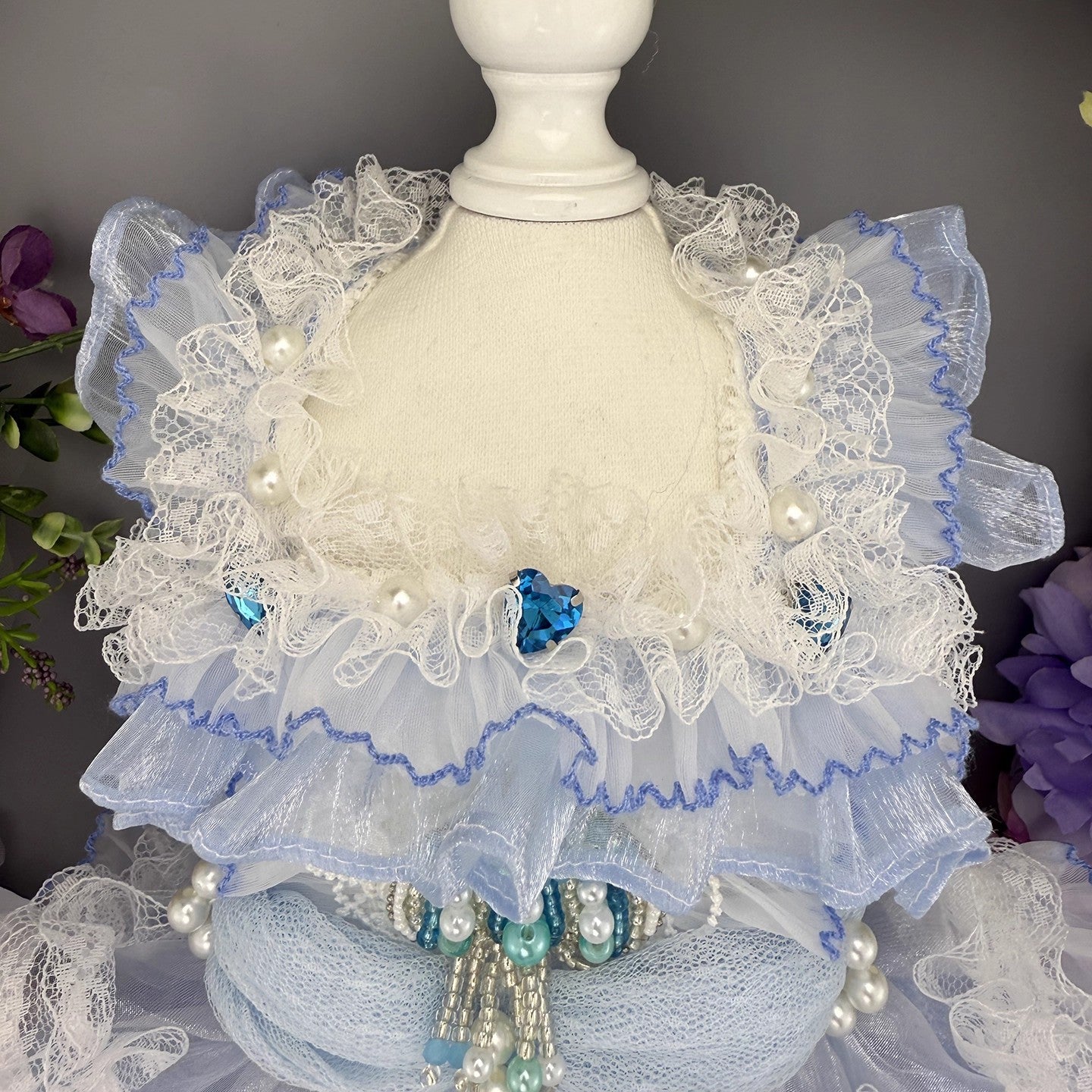 Decorative lace shawl with pearls and blue accents on a mannequin against a dark background.