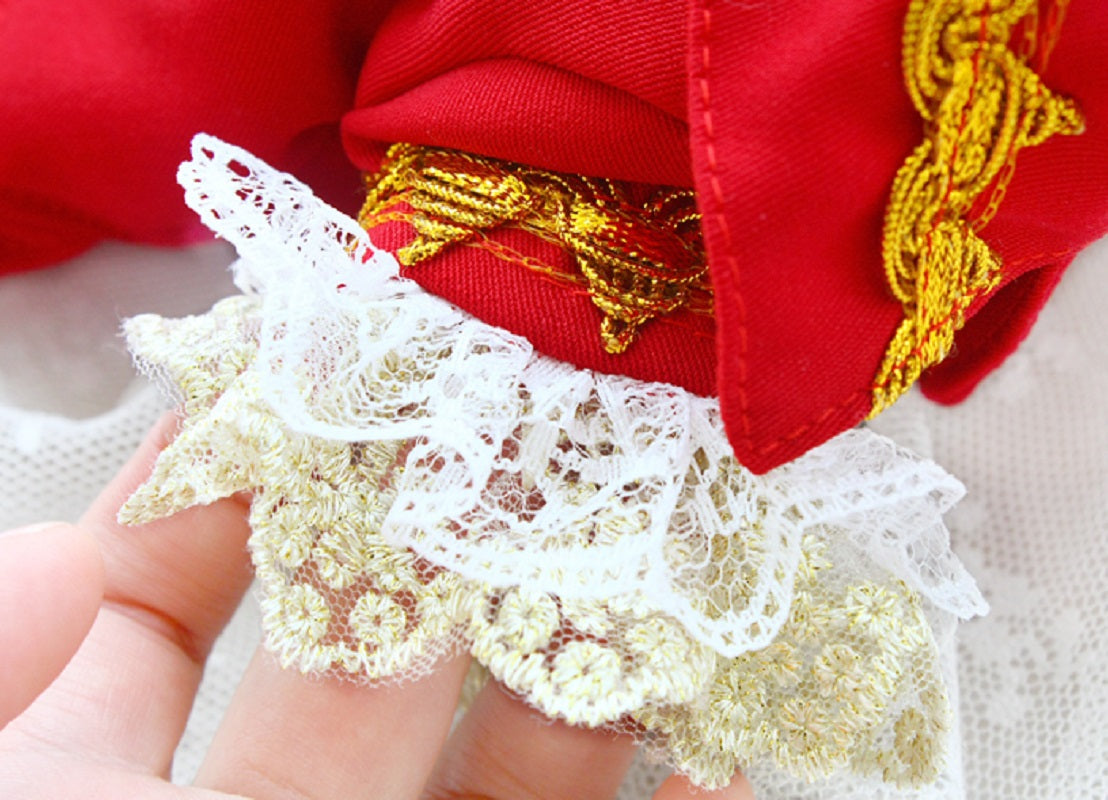 Close-up of a red garment with gold embroidery and white lace trim.
