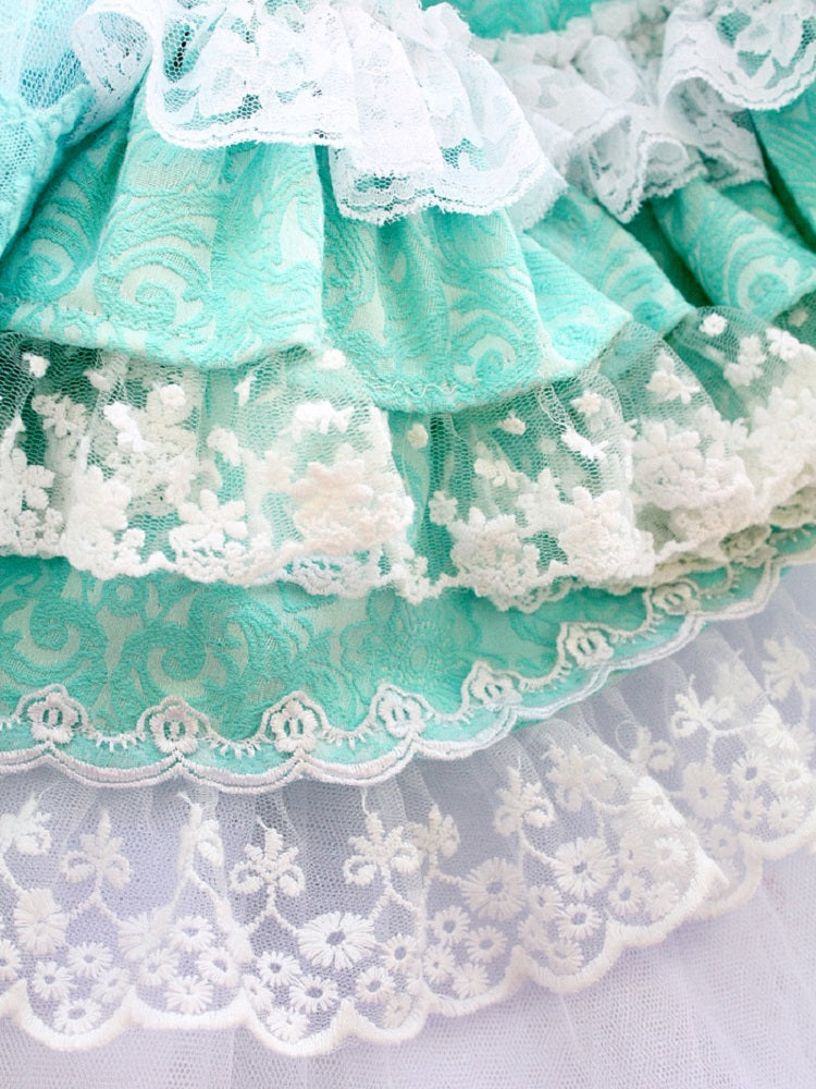 Close-up of turquoise fabric with white lace details on a light gray background