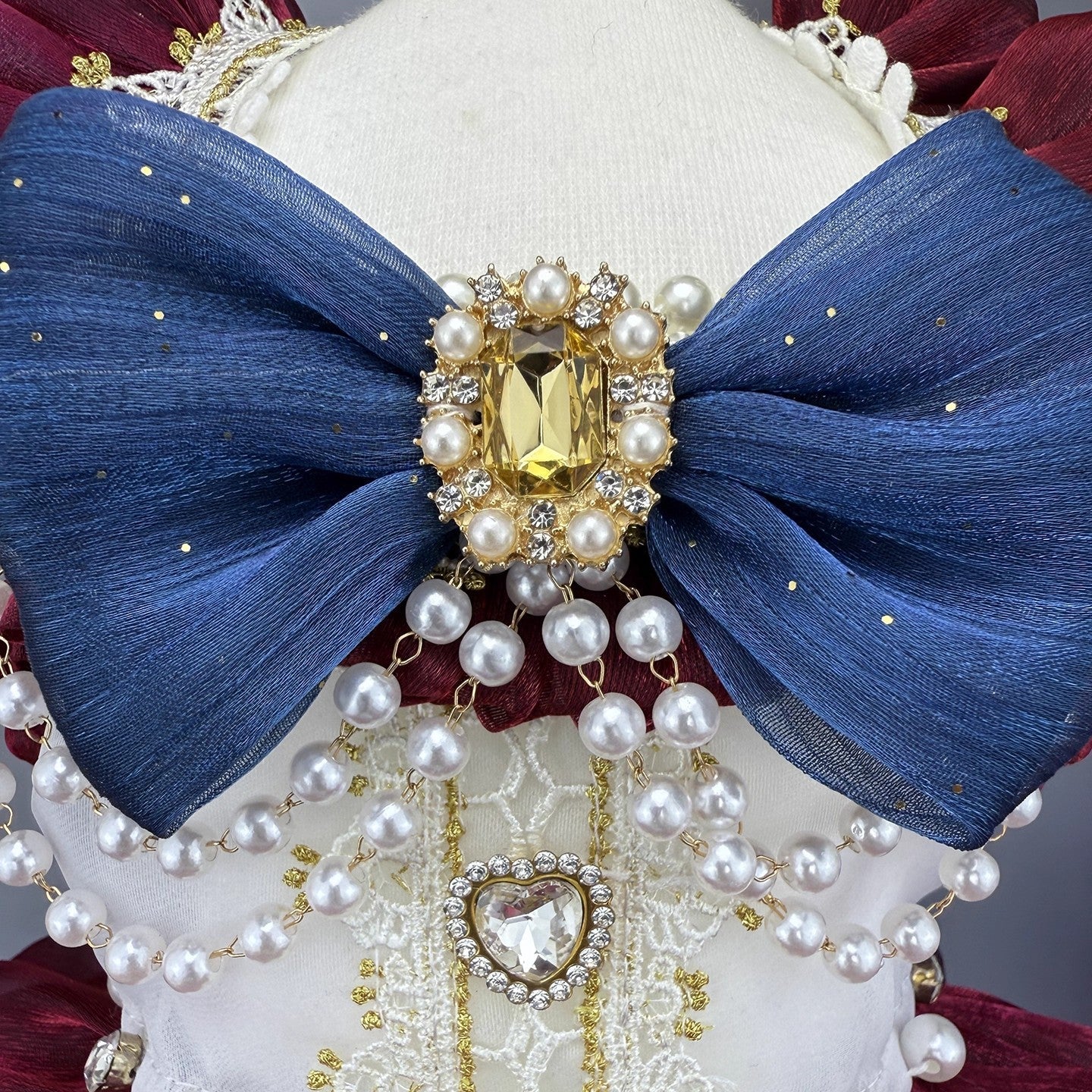 Decorative headpiece with blue bow, pearls, and gold accents on a white background
