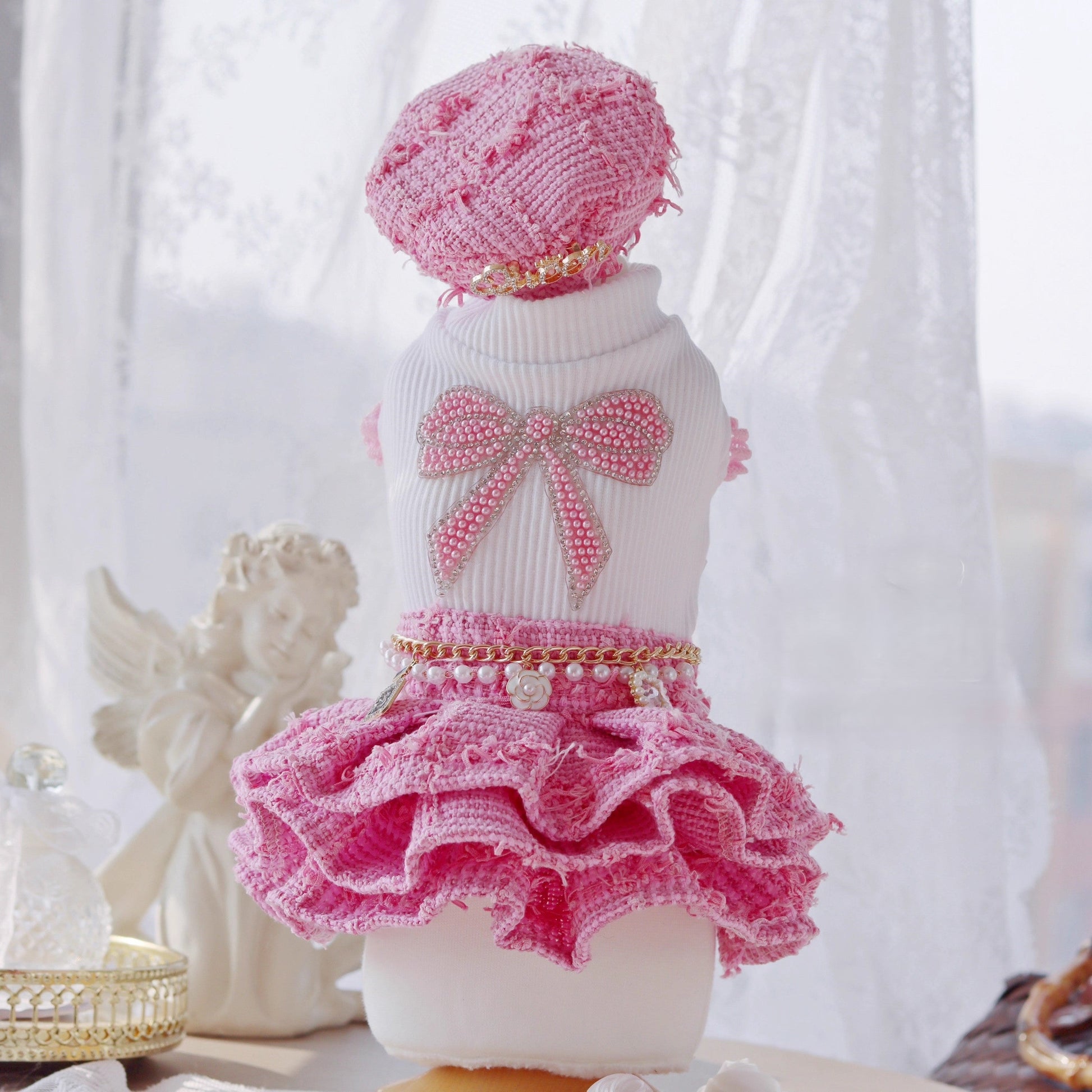 Dog wearing a pink and white outfit with a bow and ruffles on a white background