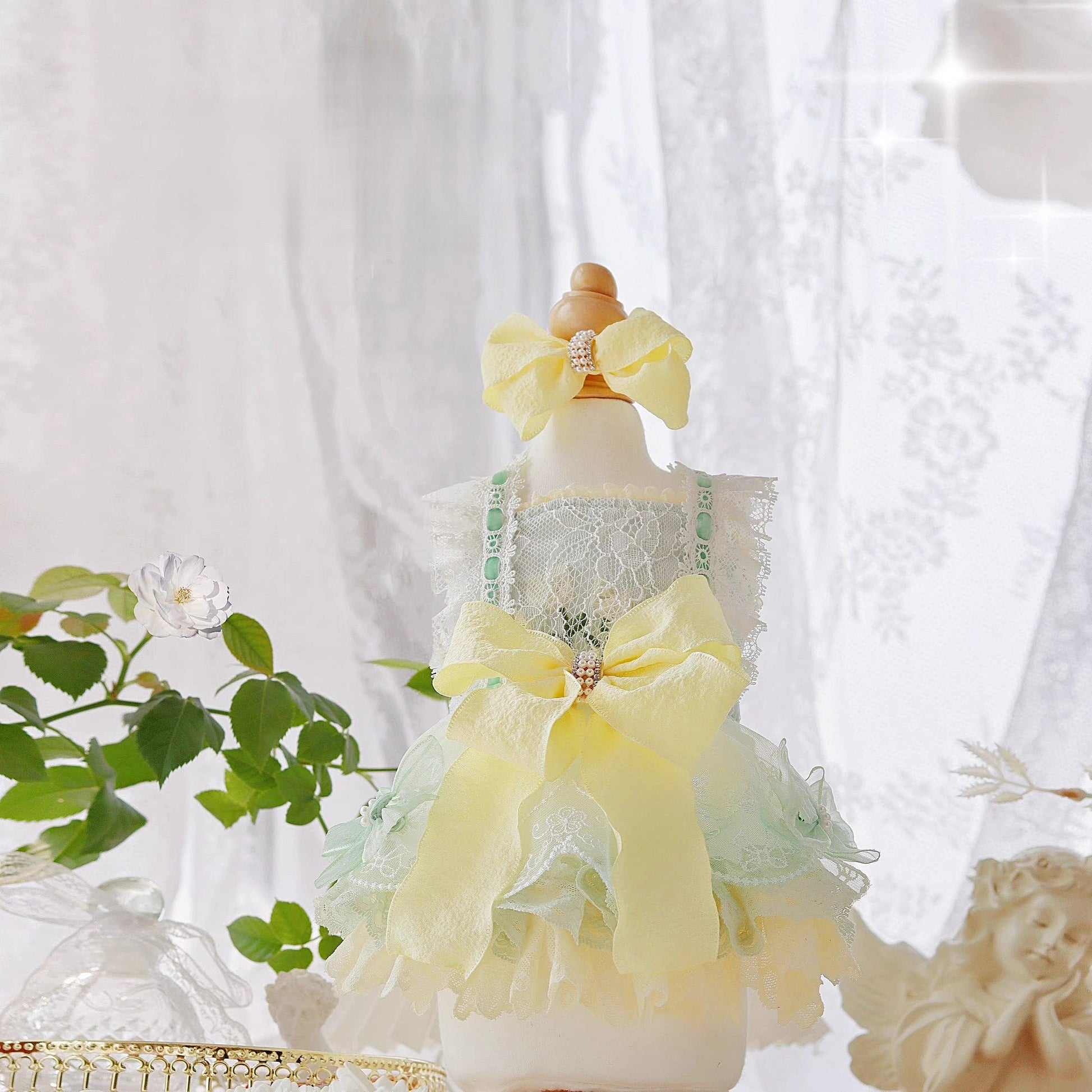 Mannequin wearing a yellow and green dress with decorative bows against a white curtain background.