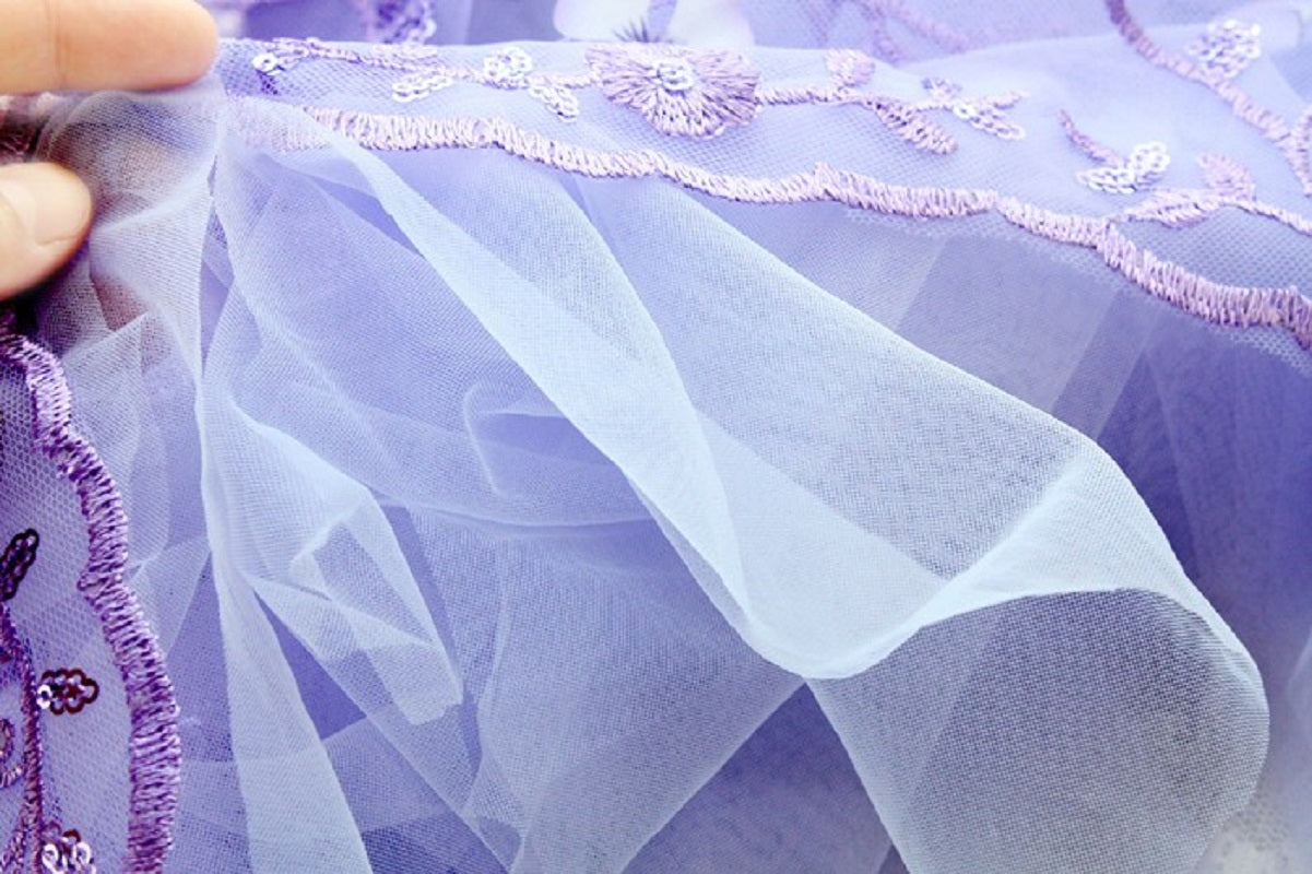 Close-up of light purple fabric with floral embroidery held by a hand.