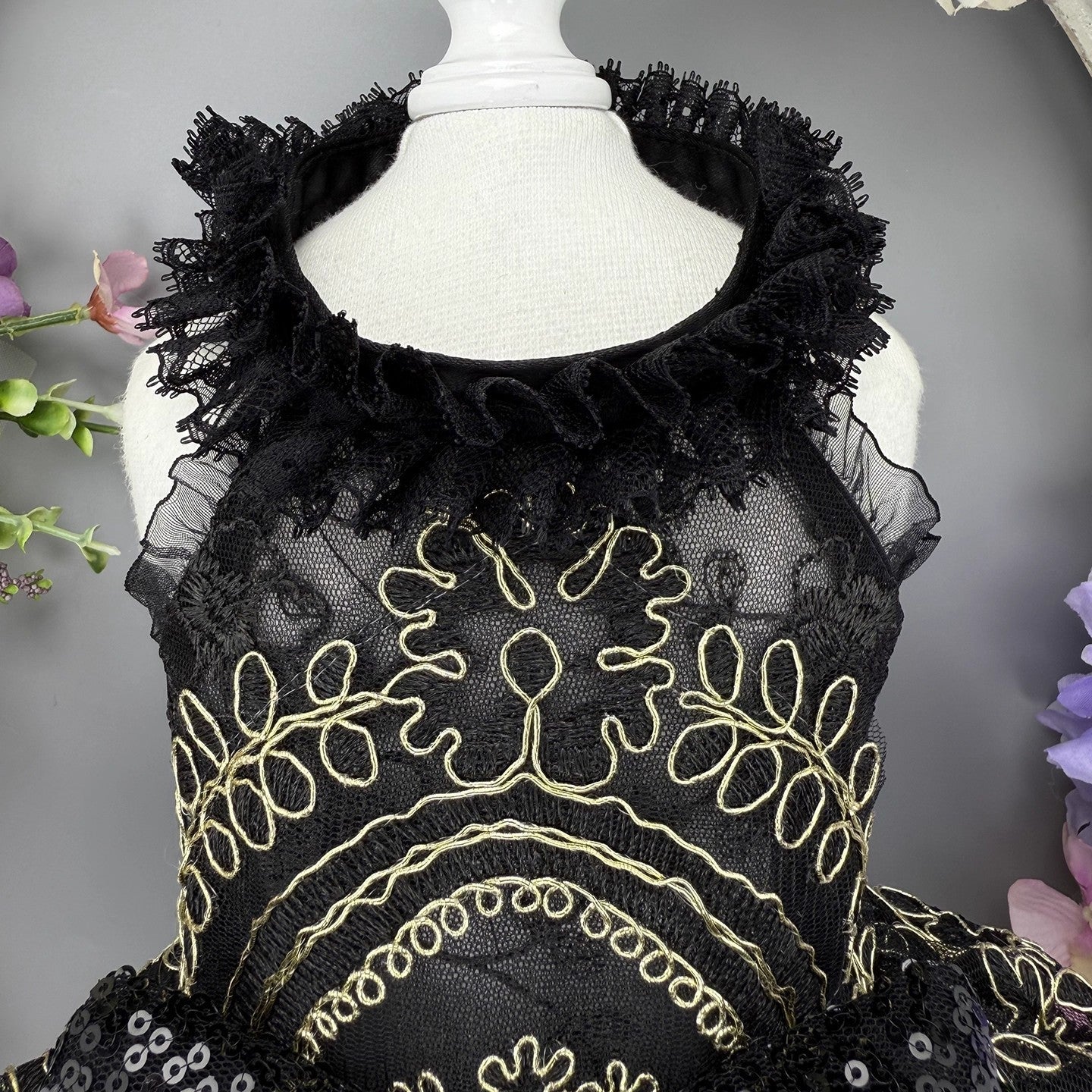 Black lace top with gold embroidery on a mannequin against a gray background