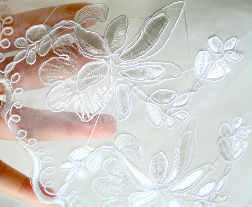 Close-up of white lace fabric with floral patterns held by a hand on a light background