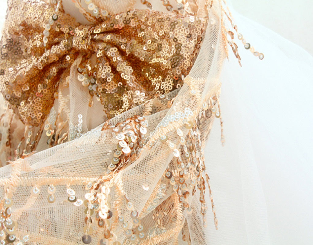 Close-up of a gold and beige sequined fabric with a bow on a light background