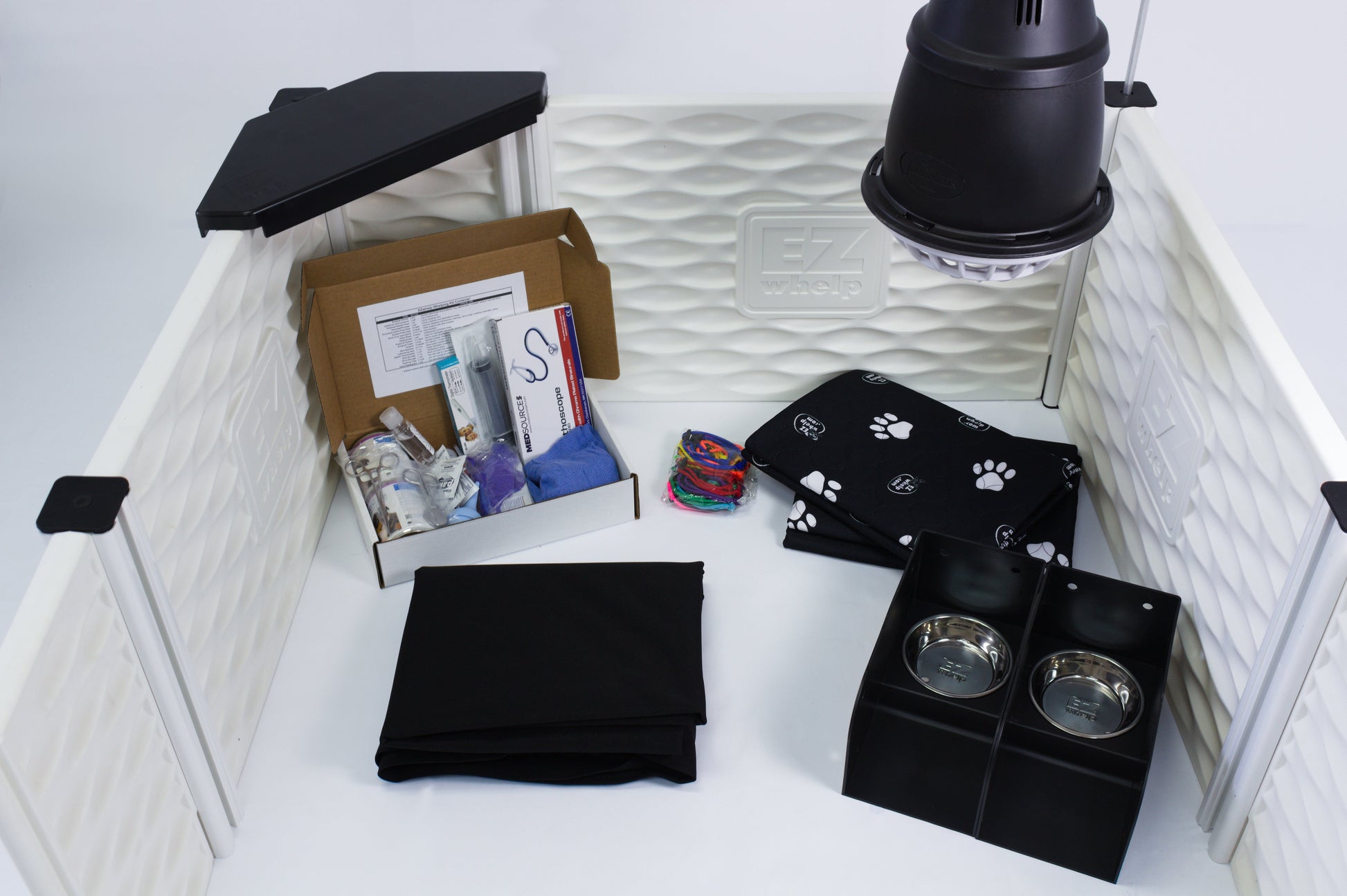 Pet supplies including a black pet bed, bowls, and a box inside a white pet pen.