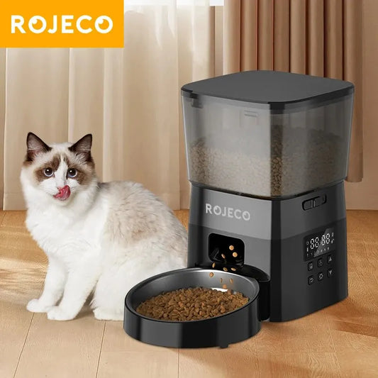 Cat sitting next to a ROJECO pet feeder on a wooden floor.