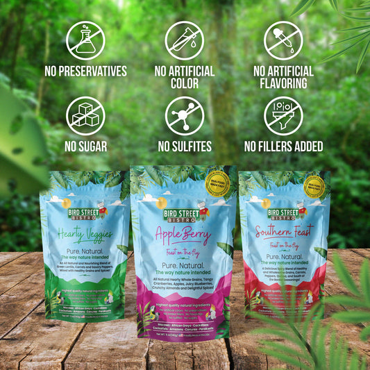 Three packages of Bird Street Bistro pet food on a wooden surface with greenery in the background.