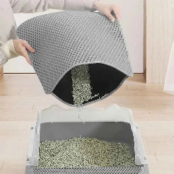 Person removing a gray cat litter mat from a litter box on a wooden floor.