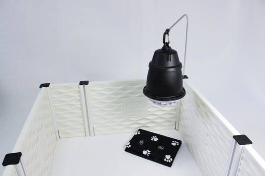Black pendant light hanging above a white pet pen with a black mat featuring paw prints on a white background.