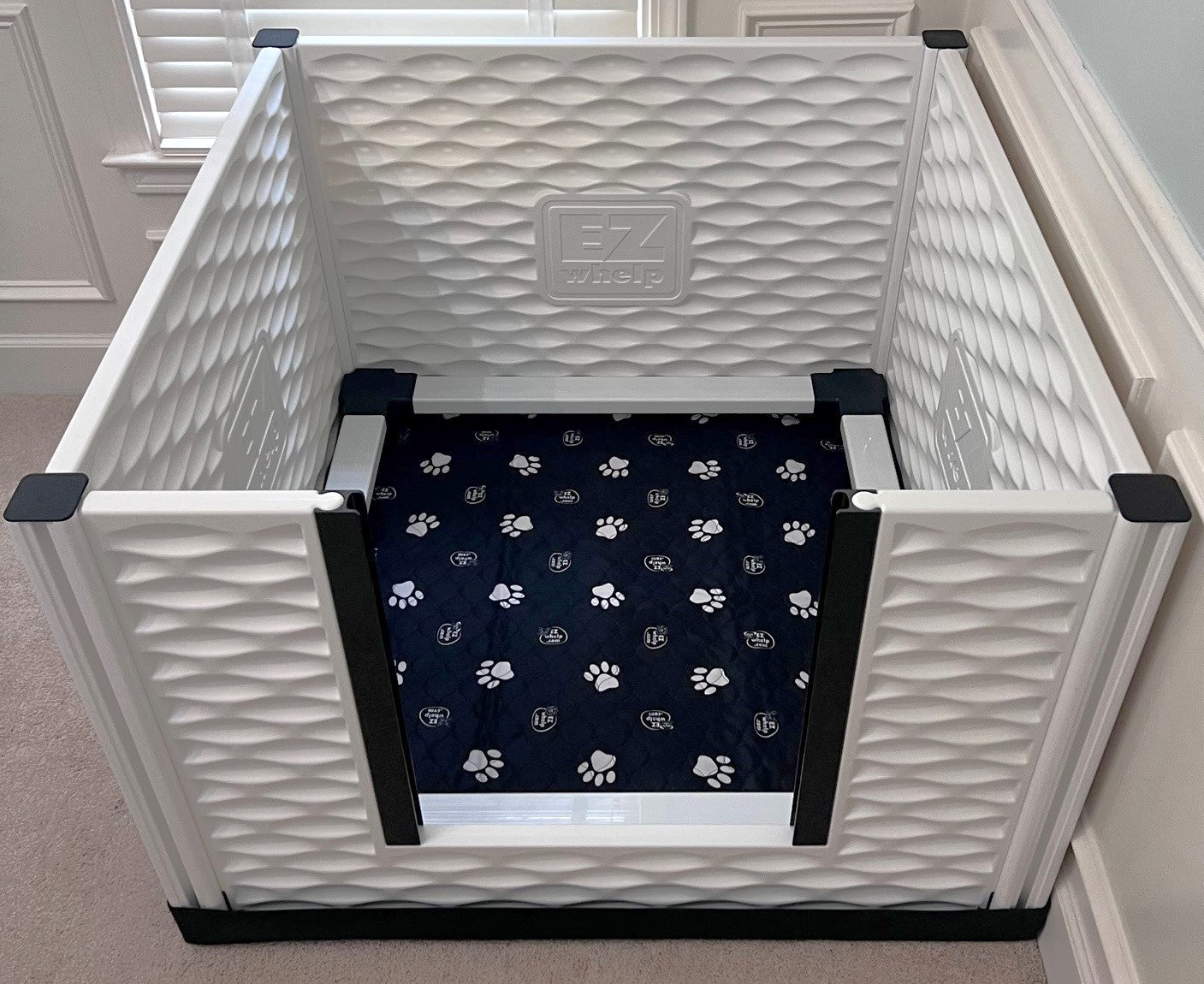 White pet crate with a dark blue mat featuring paw prints on a light-colored floor.