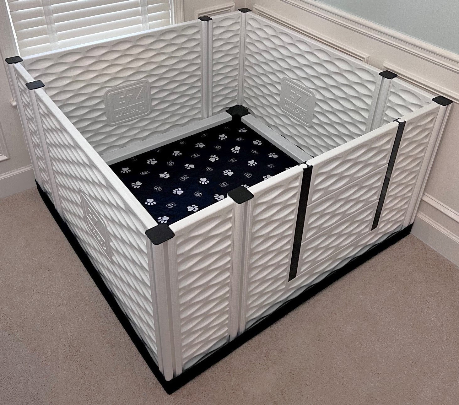 White pet playpen with a black mat inside on a carpeted floor.
