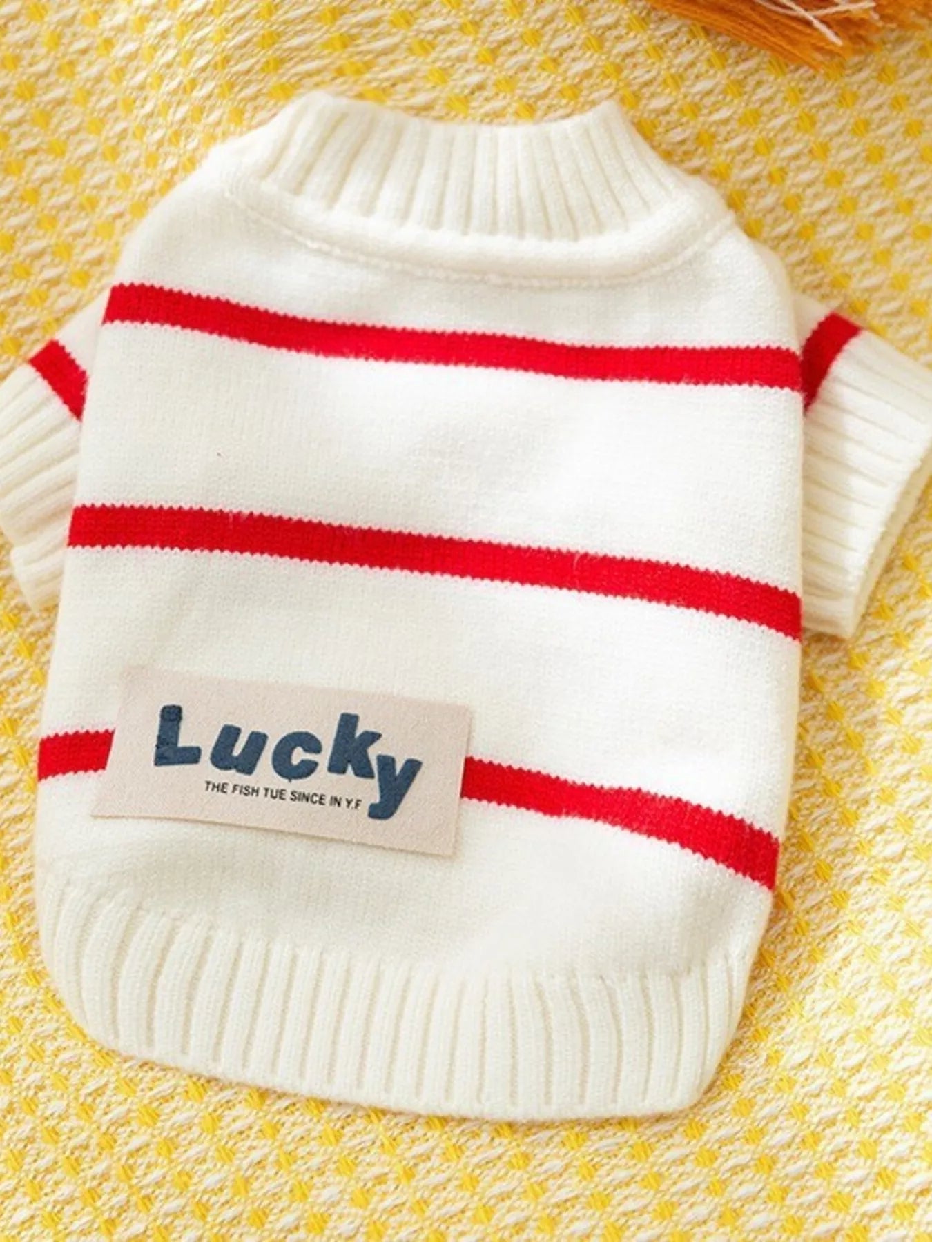 White sweater with red stripes and 'Lucky' patch on a yellow textured background