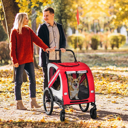 Man and woman walking a dog in a red pet stroller through a park with autumn leaves.