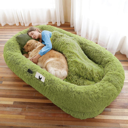 Woman and dog lying on a large green fluffy pet bed indoors.