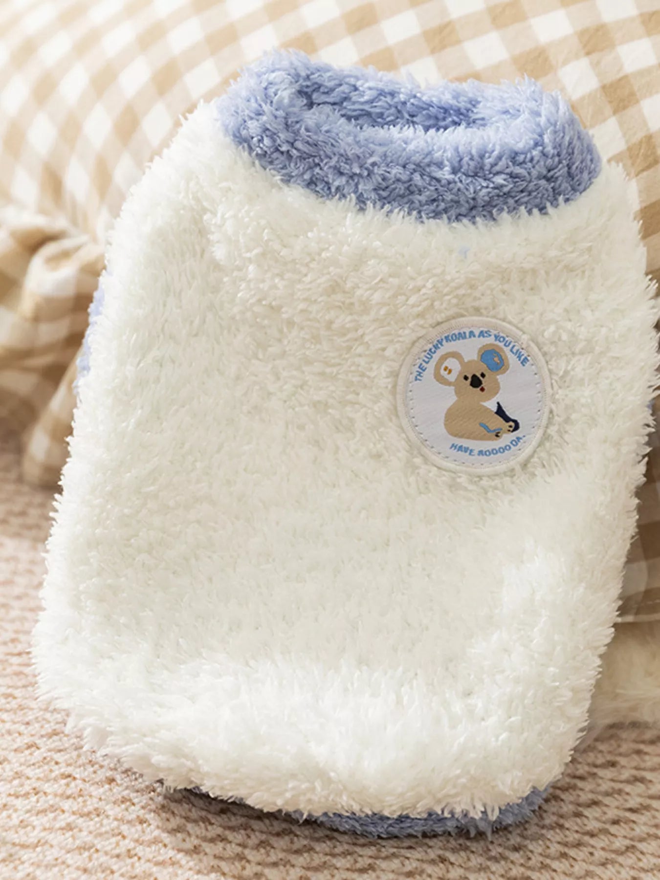 White fuzzy bottle cover with blue rim and a logo on a textured surface