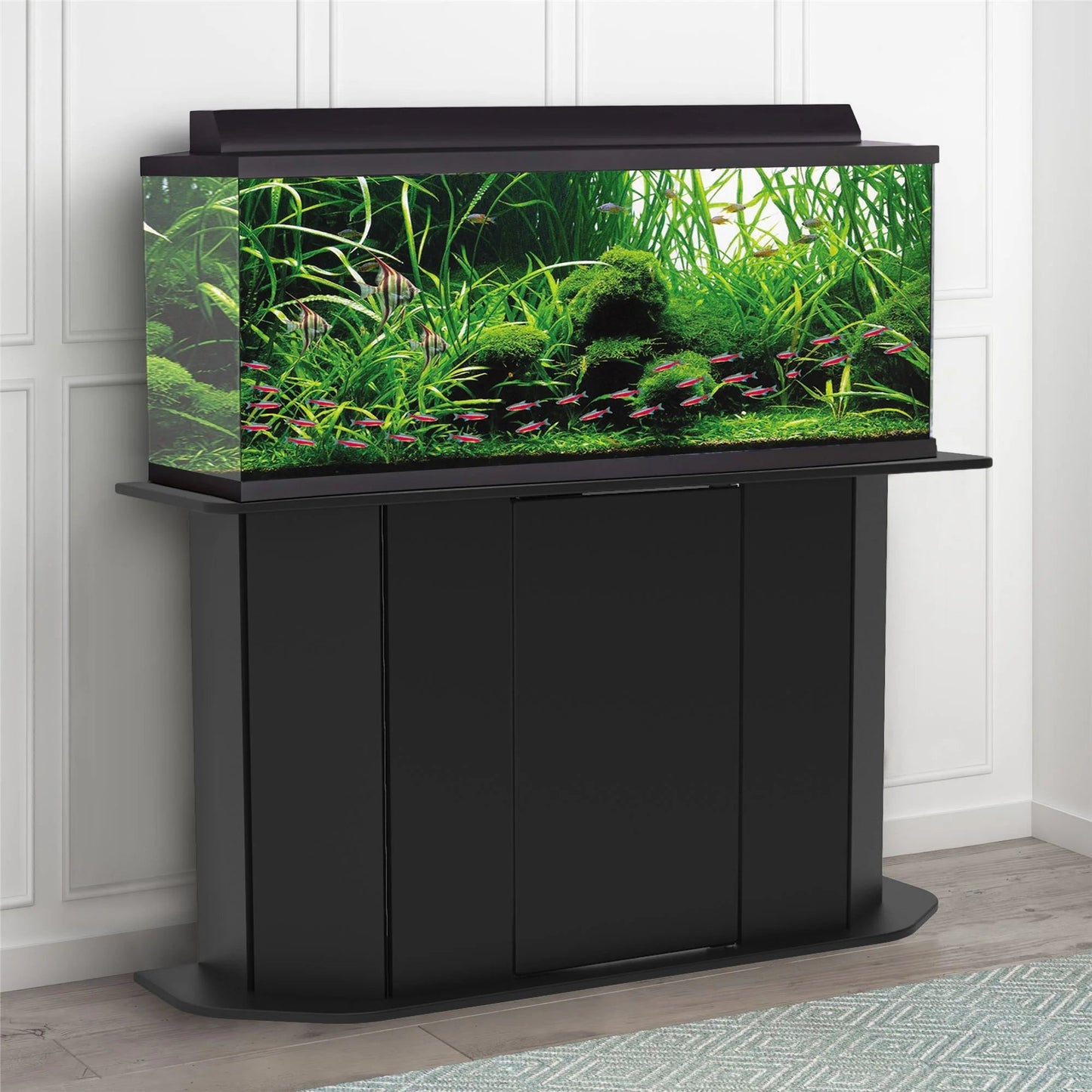 Black aquarium stand with a fish tank filled with water plants and fish on a white paneled wall background.