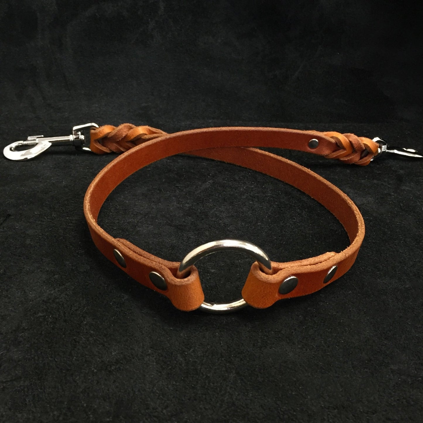 Brown leather dog collar with metal ring and clip on a black background