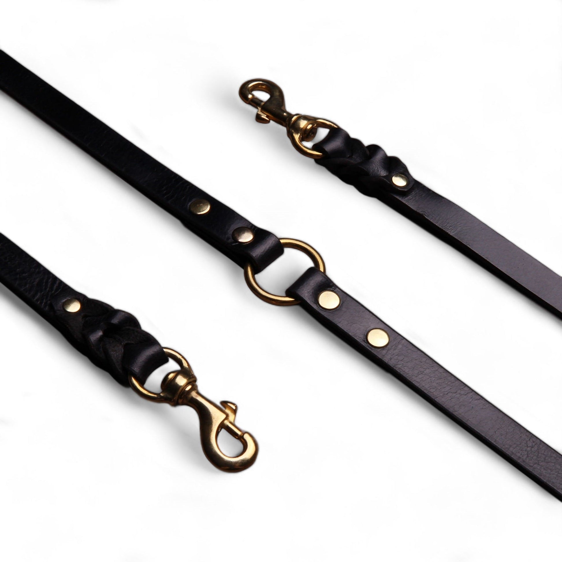 Black leather dog leashes with gold hardware on a white background