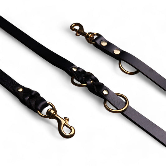 Two black leather dog leashes with gold hardware on a white background