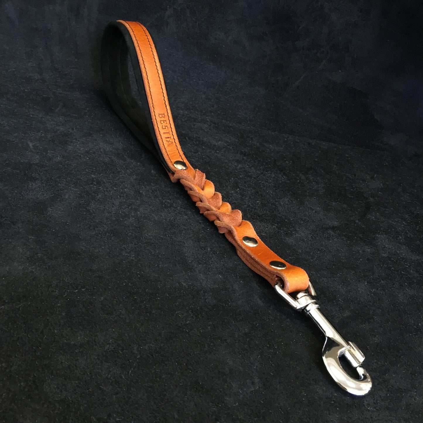 Brown leather dog leash with metal clip on a black background