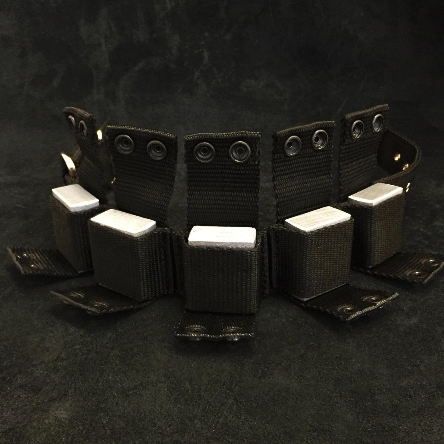 Black tactical belt with multiple pouches on a dark background