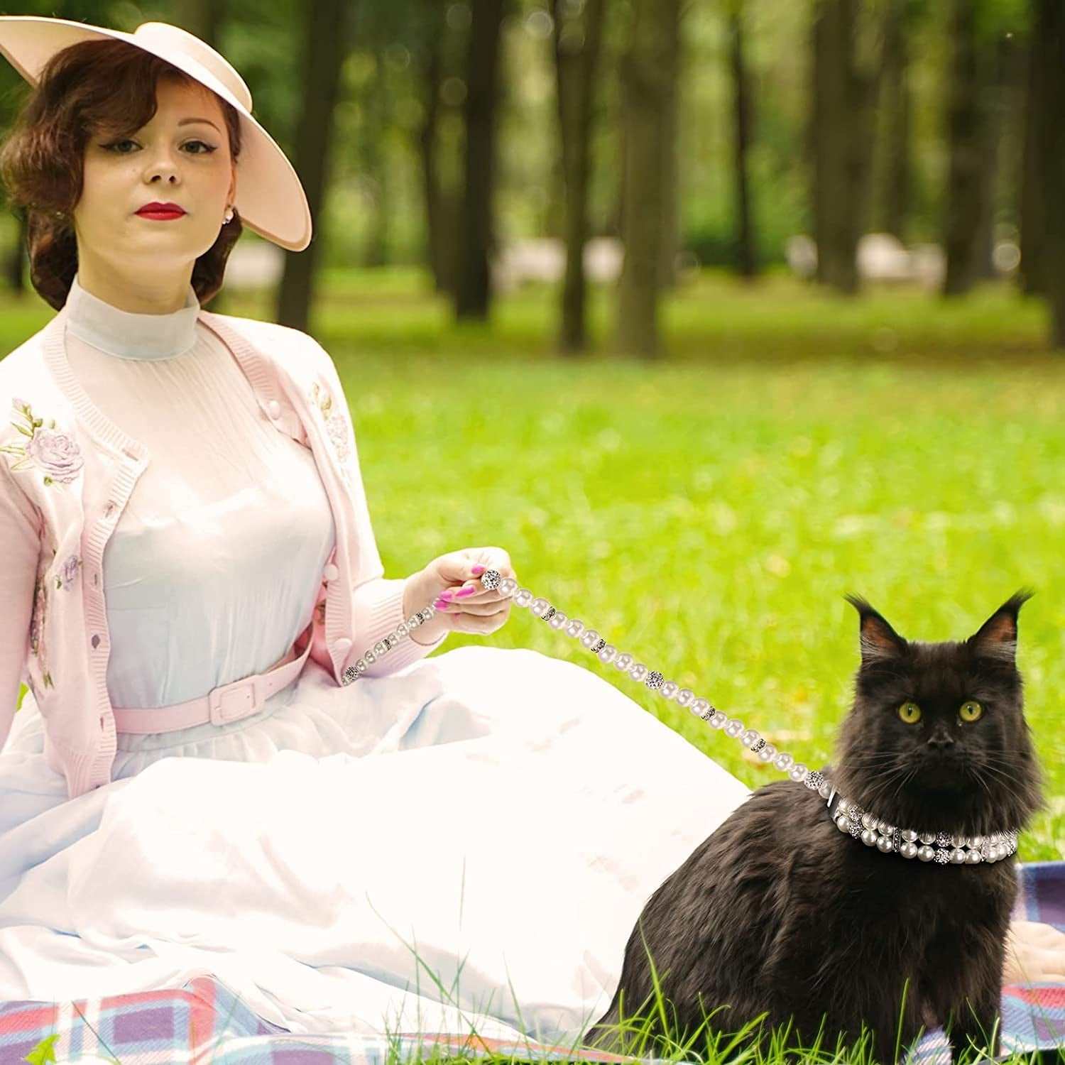 Woman in vintage attire with a black cat on a grassy field