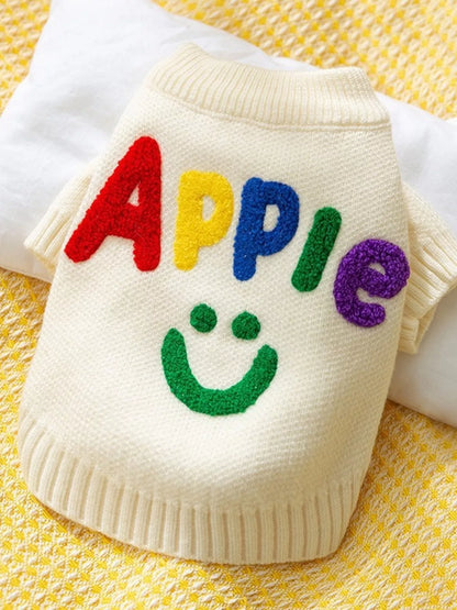 White sweater with colorful letters spelling 'APPLE' on a yellow textured background