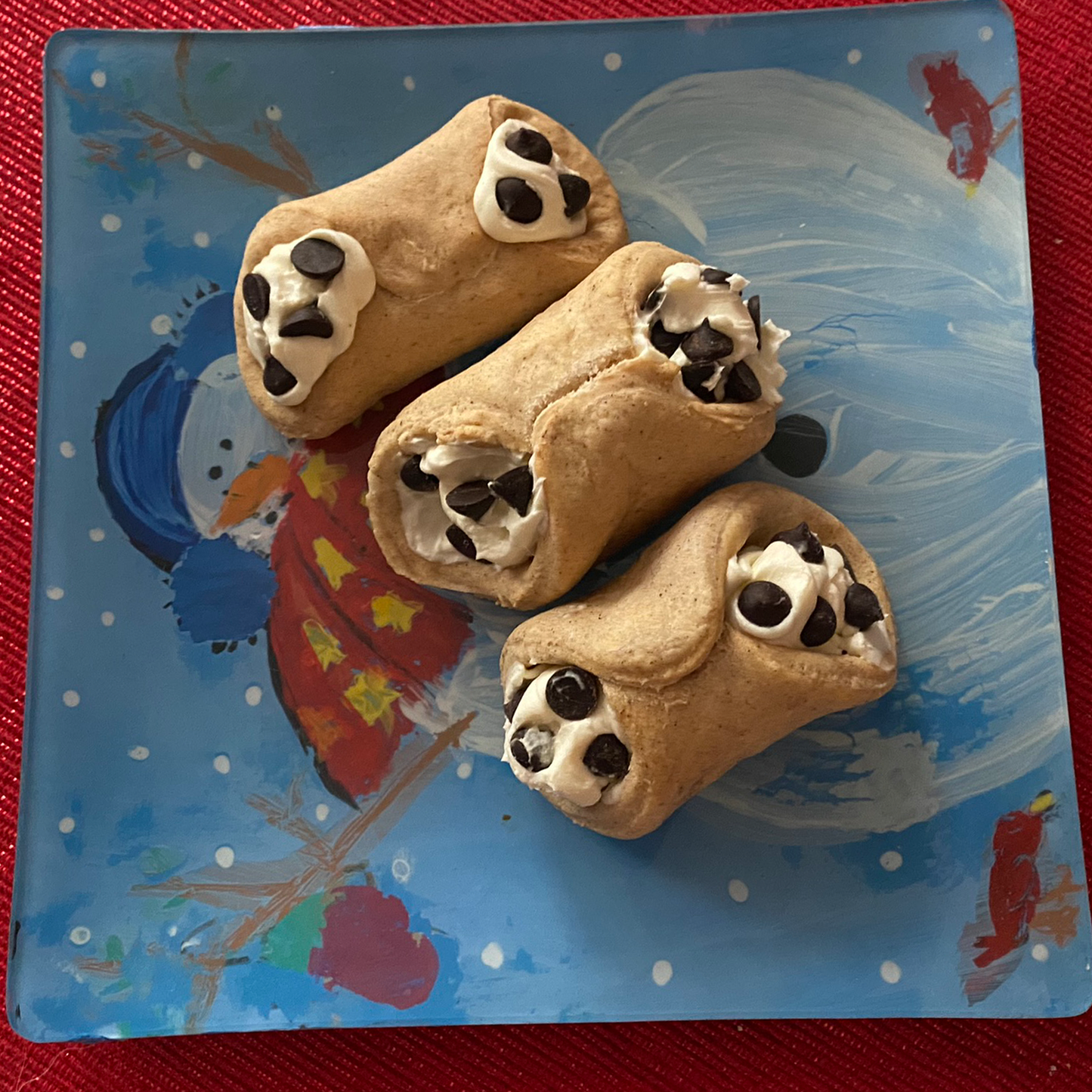 Three pastries with chocolate chips on a blue plate with a child-like drawing of a snowman.